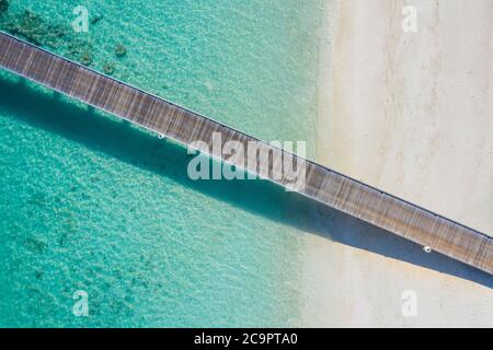 Exotische Luftaufnahme von türkisfarbenem Wasser mit hölzernen Steg auf der Malediven Insel, wunderschönes seichtes Meerwasser und Korallen mit weißem Sand. Motivierend Stockfoto