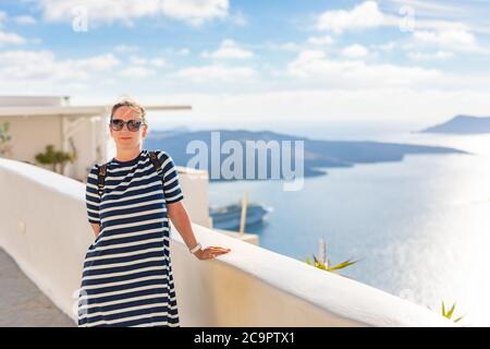 Glückliche lächelnde Frau in Kleid mit Sonnenbrille auf einem Hintergrund der weißen Häuser Architektur in Santorini. Reise Abenteuer Porträt, Blick auf die Straße Stockfoto