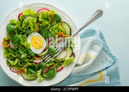 Gesunder grüner Salat mit frischem Gemüse und gekochtem Ei auf blauem Tischhintergrund Stockfoto