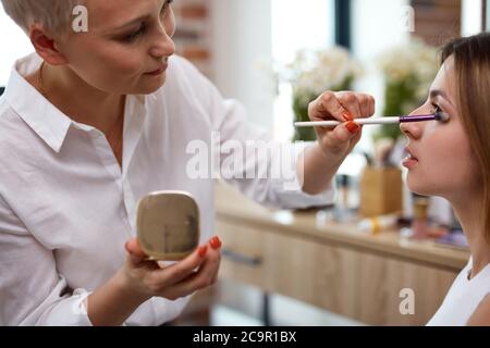 Berühmte talentierte Make-up-Künstlerin macht Make-up auf Modell, verwendet sie Pinsel für die Anwendung von Kosmetik auf Gesicht, genießen Sie die Arbeit in der Beauty-Industrie Stockfoto