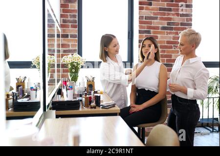 Professionelle Make-up Künstler und Friseur arbeiten zusammen im Schönheitssalon, schöne Modell kam modische Make-up und Frisur für Hochzeit zu bekommen. Stockfoto