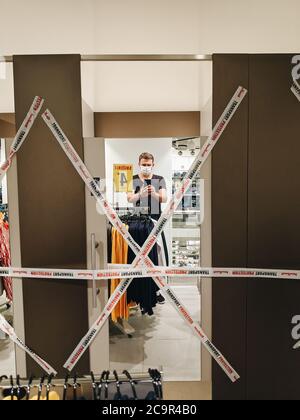 Budva, Montenegro - 01. august 2020: Ein Mann mit einer medizinischen Maske nimmt ein Selfie im Spiegel einer Garderobe in einem NewYorker Bekleidungsgeschäft, bedeckt Stockfoto