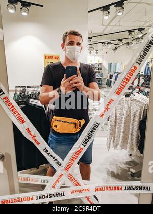 Budva, Montenegro - 01. august 2020: Ein Mann mit einer medizinischen Maske nimmt ein Selfie im Spiegel einer Garderobe in einem NewYorker Bekleidungsgeschäft, bedeckt Stockfoto