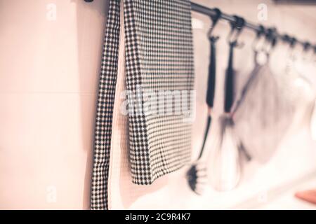 Nahaufnahme von Textilservietten, die an Metallgeländer hängen, mit verschiedenen Utensilien in der Nähe der Wand in der modernen Küche Stockfoto