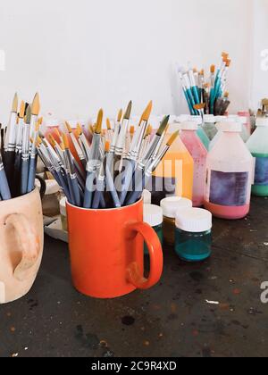 Verschiedene Pinsel und flüssige Farben in Flaschen auf dem Tisch in der modernen Werkstatt platziert Stockfoto