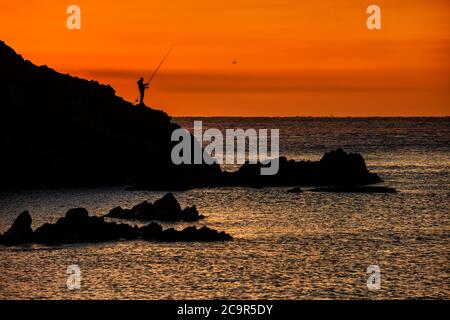 Sonnenaufgang an der Costa Brava in Spanien mit einarmer Angler auf einer Felssilhouette. Stockfoto