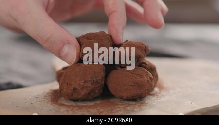Man Hand legte handgemachte Schokoladentrüffel auf ein Holzbrett Stockfoto