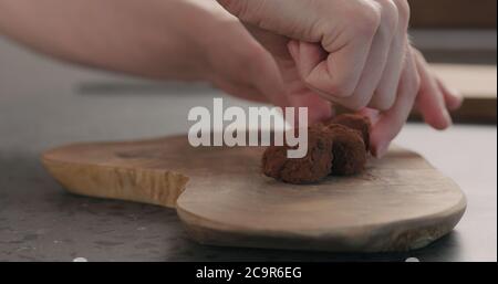 Man Hand legte handgemachte Schokoladentrüffel auf ein Holzbrett Stockfoto
