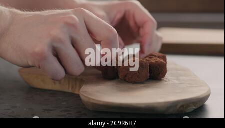 Man Hand legte handgemachte Schokoladentrüffel auf ein Holzbrett Stockfoto