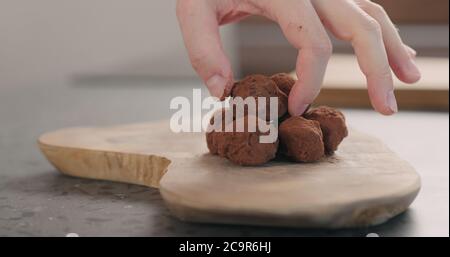 Man Hand legte handgemachte Schokoladentrüffel auf ein Holzbrett Stockfoto