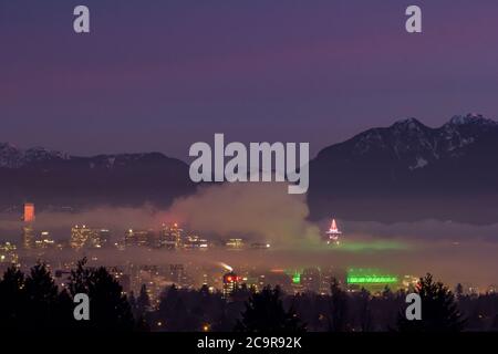 Vancouver's Skyline bei Nacht - Luftblick von den Queens Elizabeth Park im Winter mit verschneiten Bergen im Hintergrund Stockfoto