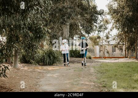 Zwei kaukasischen Kinder reiten Roller mit Masken während der Corona COVID-19 Pandemie Stockfoto