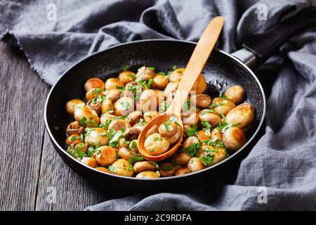 Sautierten Knoblauch weißen Pilzen mit Petersilie, Zitronensaft genannt al ajillo in Spanien gerösteten Knoblauch Champignons serviert auf einer Pfanne auf einem hölzernen Hintergrund, Stockfoto