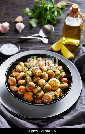 Keto Diät spanisches Gericht: Gerösteter Knoblauch Champignon Pilze al ajillo mit gehackter Petersilie auf einem schwarzen Teller auf Holztisch mit Zutaten: Olive oi Stockfoto