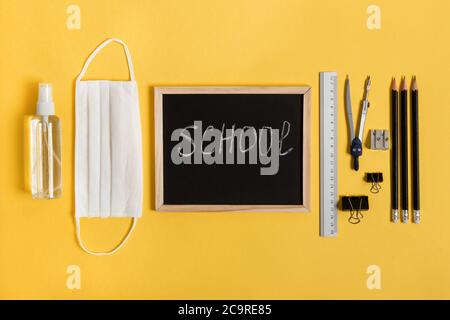 Tafel mit Schul- und Bürobedarf auf gelbem Hintergrund Draufsicht während der Coronavirus-Zeit. Zurück zur Schule Konzept. Stockfoto