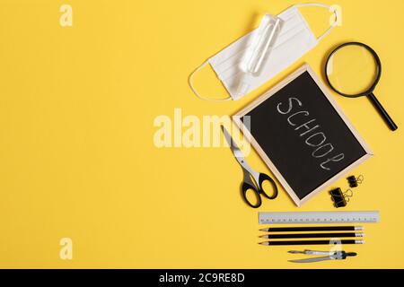Tafel mit Schul- und Bürobedarf auf gelbem Hintergrund Draufsicht während der Coronavirus-Zeit. Zurück zur Schule Konzept. Speicherplatz kopieren. Stockfoto