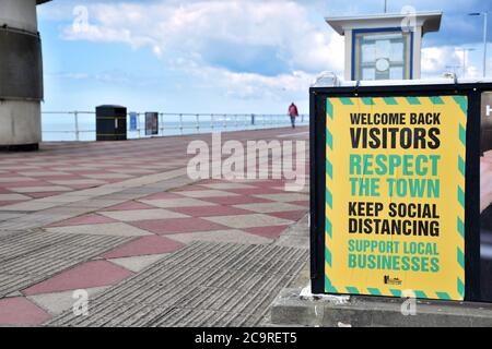 Ein Plakat, das Besucher nach dem Ende der Covid 19-Sperre in Hastings willkommen heißt, aber die Menschen auffordert, soziale Distanzierung beizubehalten. Stockfoto