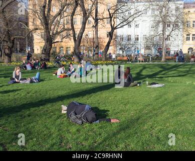 Tschechische Republik, Prag, 10. April 2018: Schlafender Mann und Gruppe von Menschen entspannen auf üppigem grünen Gras und genießen Sie den frühen Frühlingstag auf Karlinske Stockfoto