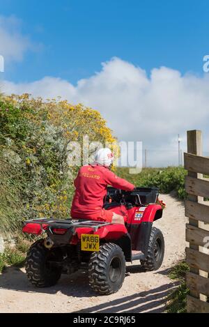 Ein RNLI Rettungsschwimmer auf einem Quad-Bike entlang des Küstenweges bei Fistral in Newquay in Cornwall. Stockfoto