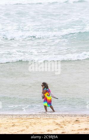 Ein Urlauber in einem farbenfrohen Kleid, der an der Uferlinie am Fistral Beach in Newquay in Cornwall steht. Stockfoto