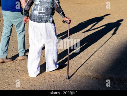 Neuhardenberg, Deutschland. August 2020. Zwei ältere Menschen gehen Hand in Hand mit einem Gehstock über einen Pfad und werfen einen langen Schatten. Quelle: Patrick Pleul/dpa-Zentralbild/ZB/dpa/Alamy Live News Stockfoto