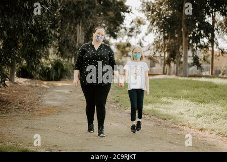 Mutter und Tochter tragen Stoffmasken während der Coronavirus COVID-19 Pandemie gehen zu Fuß Stockfoto