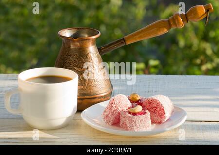 Türkischer Genuss, Kaffeetasse und der Cezve im Sonnenlicht auf einem Hintergrund von grünem, angenehmen Abend Stockfoto