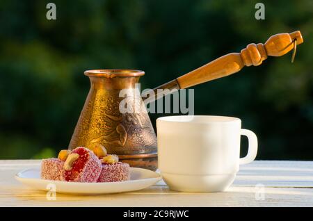 Rakhat Lokum, Cezve und eine Tasse Kaffee im Sonnenlicht, auf einem Hintergrund von Grün Stockfoto