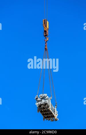 Der Haken des Turmdrehkrans hebt die Fracht von den Holzrohren, nah oben vor dem Hintergrund des Himmels. Stockfoto