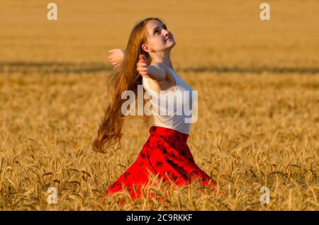 Mädchen im roten Rock wirbeln in Weizenfeld Arme ausgebreitet Stockfoto