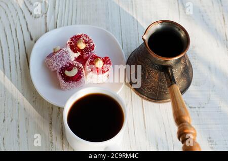 Blick von oben auf einen Kaffee, türkische Delight und Töpfe in der Sonne auf einem weißen Holzhintergrund Stockfoto