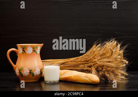 Krug, ein Glas Milch, ein Laib und eine Garbe Ohren auf schwarzem Hintergrund Stockfoto