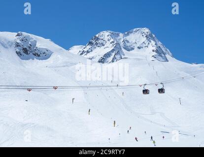 Stubaier Gletscher, ÖSTERREICH, 2. Mai 2019: Winterlandschaft mit oranger Bergbahn und schneebedeckten Berghängen und Pisten mit Skifahrern im Skigebiet Stockfoto