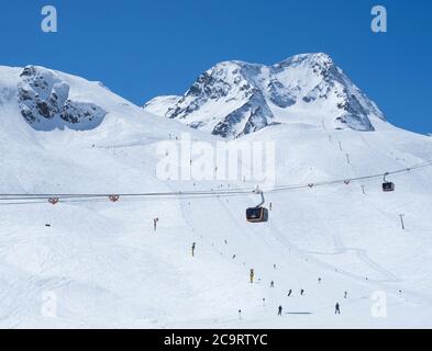 Stubaier Gletscher, ÖSTERREICH, 2. Mai 2019: Winterlandschaft mit oranger Bergbahn und schneebedeckten Berghängen und Pisten mit Skifahrern im Skigebiet Stockfoto