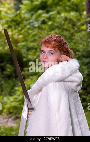 Porträt einer rothaarigen Frau mit elfigen Ohren und weißem Mantel, der ein Schwert in der Hand hält. Stockfoto
