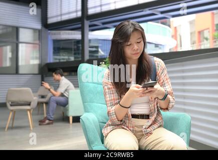 Junge chinesische Mädchen mit einem Mann hinter ihr mit Handy für SMS oder Online-Lesen. Digitale Lebenszytäre. Stockfoto