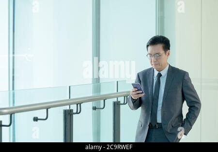 Chinesischer Geschäftsmann in Anzug und Krawatte, mit seinem Handy. Stockfoto