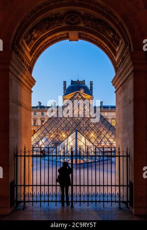 Eine Silhouette eines Touristen, der ein Bild von der beleuchteten Glaspyramide im Louvre Museum, Paris macht Stockfoto