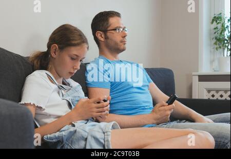 Eine gewöhnliche moderne Familie. Papa schaut fern, Tochter spielt auf dem Smartphone. Stockfoto