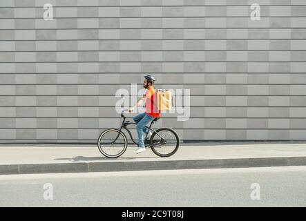 Lieferer auf dem Fahrrad. Junger Mann mit Bart und großen Rucksack reitet entlang Weg in der Stadt Stockfoto