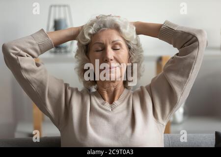 Ältere Frau legt die Hände hinter den Kopf, die im Wohnzimmer ruhen Stockfoto