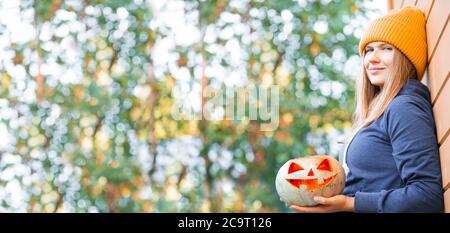 Frau in legerer Kleidung und Hut hält Halloween Kürbis über Herbst Natur Hintergrund mit Kopie Platz für Text Stockfoto