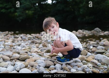 Vier Jahre alter Junge spielt neben dem Bach auf Kiesstrand Stockfoto