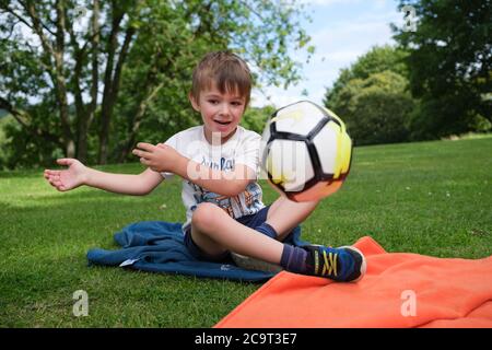 Der vierjährige Junge saß auf dem Gras und warf einen Ball Stockfoto