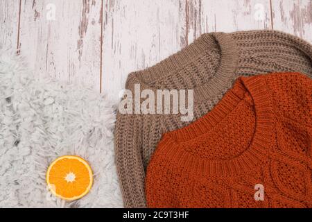 Zwei Strickpullover auf Holzuntergrund. Orange auf Fell. Modisches Konzept, Nahaufnahme Stockfoto