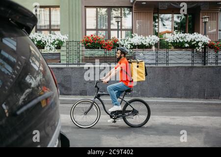 Arbeitstag Kurier in der Stadt. Junger Mann im Schutzhelm mit Rucksack fährt auf dem Fahrrad auf der Straße Stockfoto