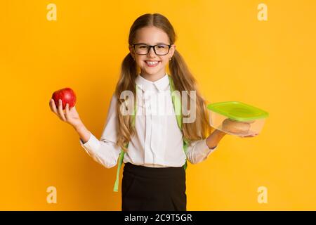 Happy Schoolgirl Holding Lunchbox Und Apfel Stehen Im Studio Stockfoto