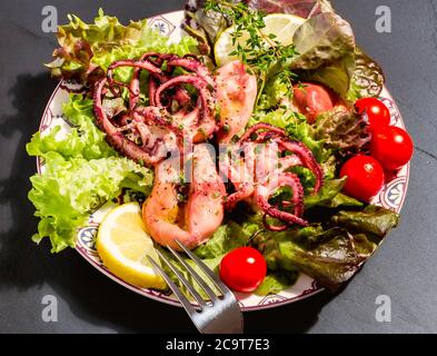 Octopus auf blauem Teller mit Salat und Zitrone, auf schwarzem Schiefer Stockfoto