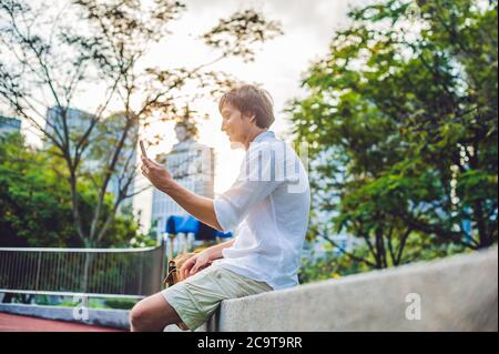 Junger Mann am Telefon. Dressing in einem weißen Hemd, beige Shorts. Mobile Office-Konzept Stockfoto