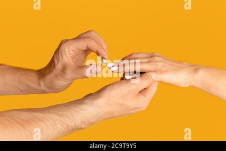 Junger Mann, der Verlobungsring auf den Finger seiner Braut über orangenen Hintergrund legt, Nahaufnahme Stockfoto